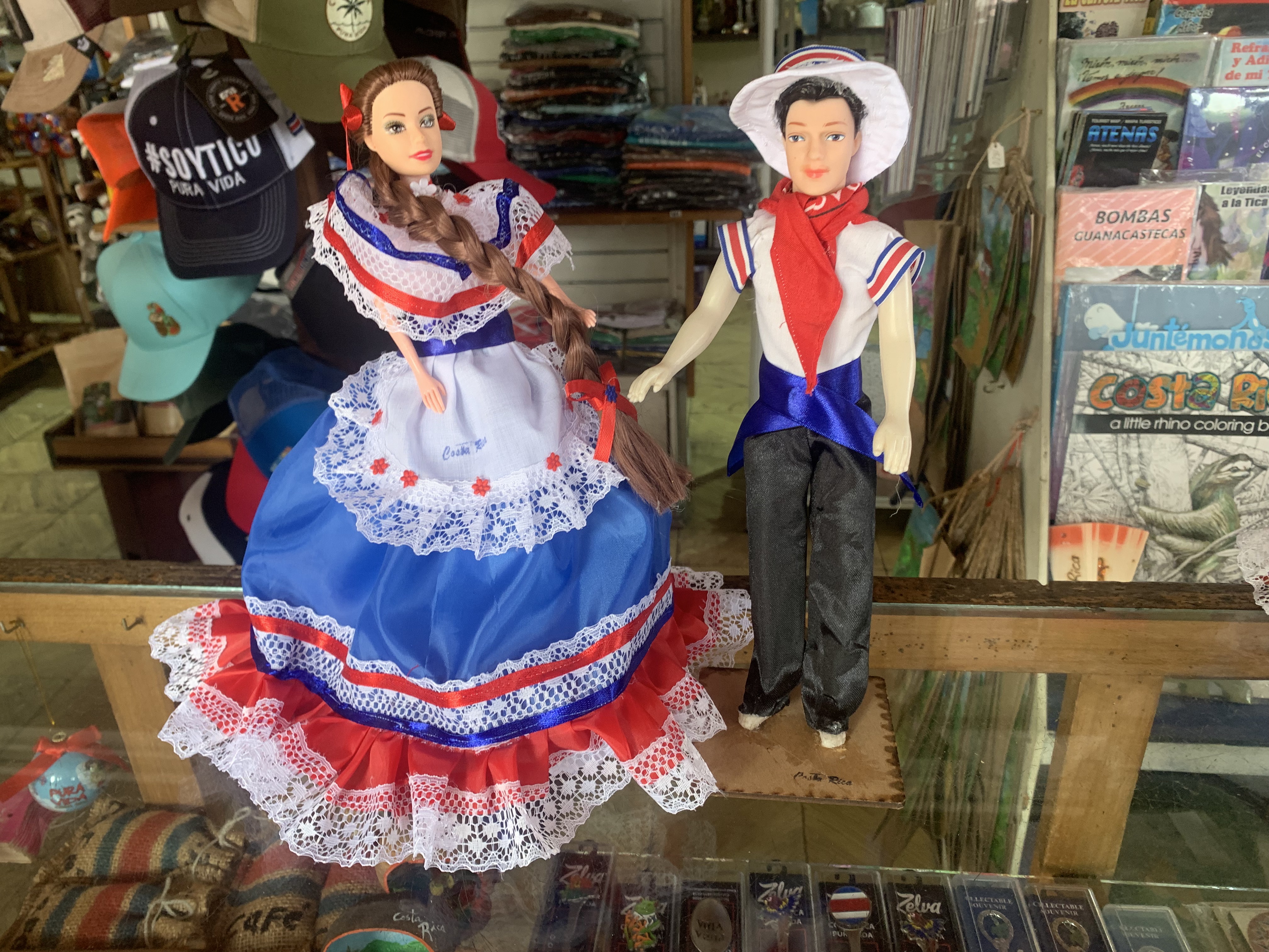 Two decorative dolls in traditional costumes displayed in a collection showcase, wearing vibrant red, white, and blue period dress with lace details.