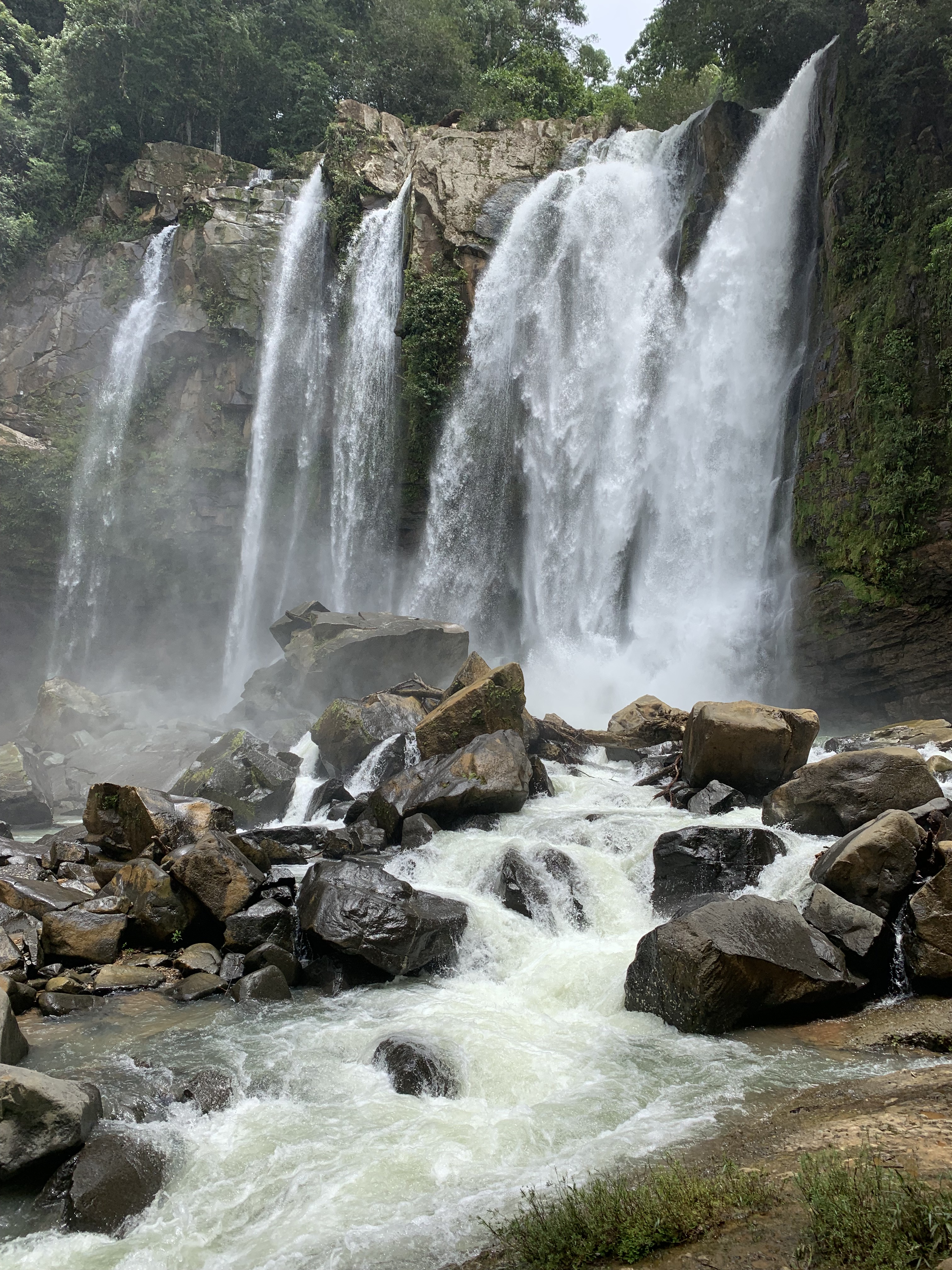 A flowing waterfall cascades gracefully over moss-covered rocks, its waters creating a gentle mist in the surrounding air. The scene captures the timeless movement of nature—constant transformation and renewal.